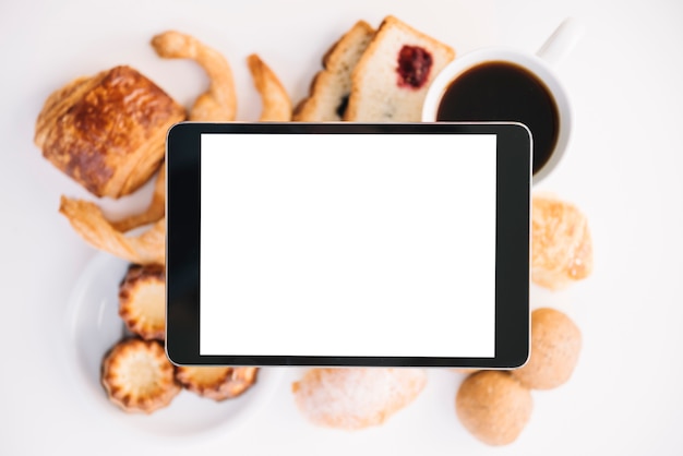 Foto gratuita tableta con pantalla en blanco encima de café con panadería