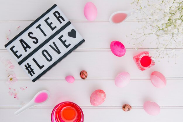 Foto gratuita tableta con el título de amor de pascua cerca de los huevos entre la ramita de flores y las latas con tinte líquido