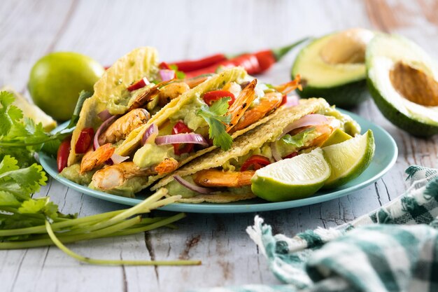 Tacos mexicanos con camarones, guacamole y verduras en mesa de madera