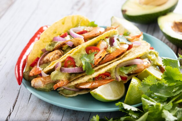 Tacos mexicanos con camarones, guacamole y verduras en mesa de madera