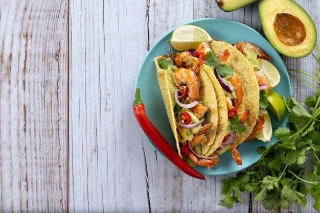 Tacos mexicanos con camarones, guacamole y verduras en mesa de madera