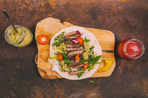 Foto gratuita tacos mexicanos con carne de res; verduras frescas y guacamole con salsa de salsa sobre fondo oxidado