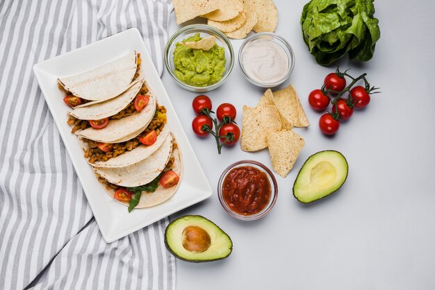 Tacos en el plato entre la servilleta junto a las salsas y verduras