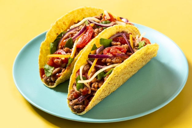 Tacos tradicionales mexicanos con carne y verduras sobre fondo amarillo