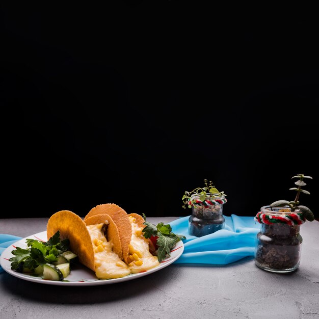 Tacos entre las verduras en el plato cerca de las plantas de interior y la servilleta en la mesa