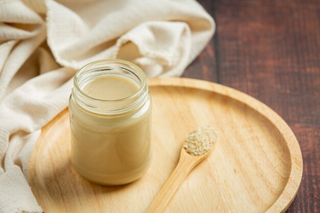 Tahini y semillas de sésamo sobre fondo de madera oscura.