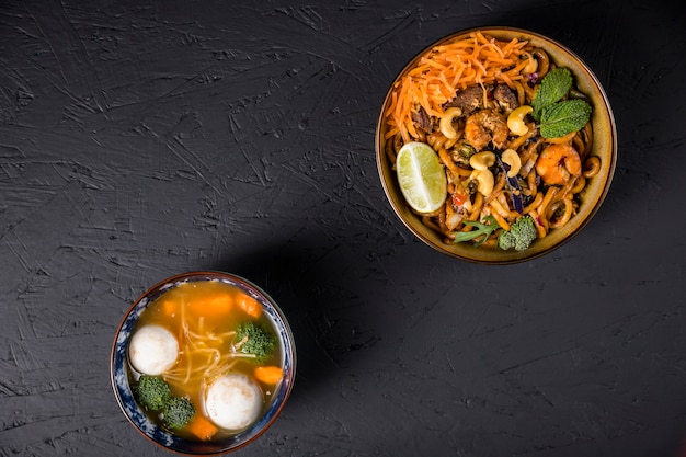 Foto gratuita los tallarines fritos del udon con la bola de pescados y la sopa de verduras en el hormigón negro texturizaron el fondo