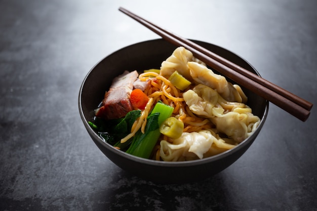 Tallarines de huevo con cerdo y wonton asados rojos en la tabla.