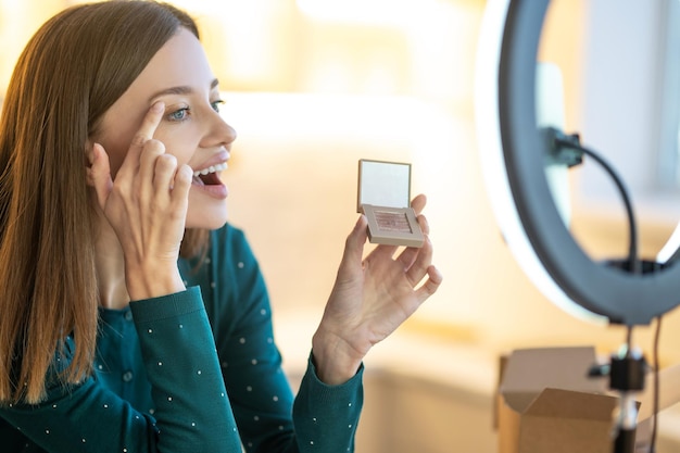 Taller de belleza. Mujer sonriente joven que muestra nuevas sombras de ojos a la audiencia en línea