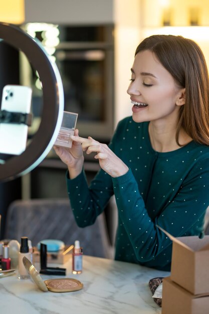 Taller de belleza. Mujer sonriente joven que muestra nuevas sombras de ojos a la audiencia en línea