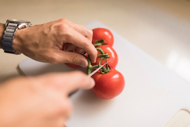 Tallo de corte de mano del hombre de tomates rojos con cuchillo afilado