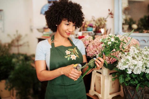 Foto gratuita tallo de corte de mujer joven de flores con tijeras de podar en tienda de flores