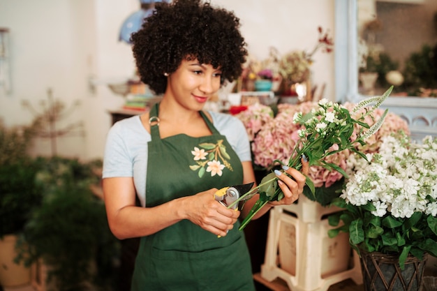 Tallo de corte de mujer joven de flores con tijeras de podar en tienda de flores