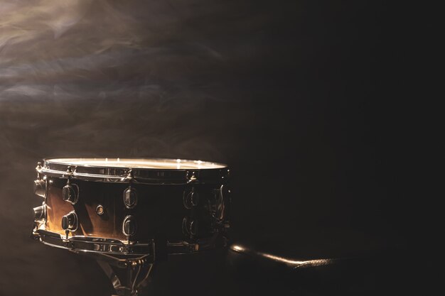 Tambor sobre fondo negro, instrumento de percusión en la oscuridad con humo de escenario, espacio de copia.