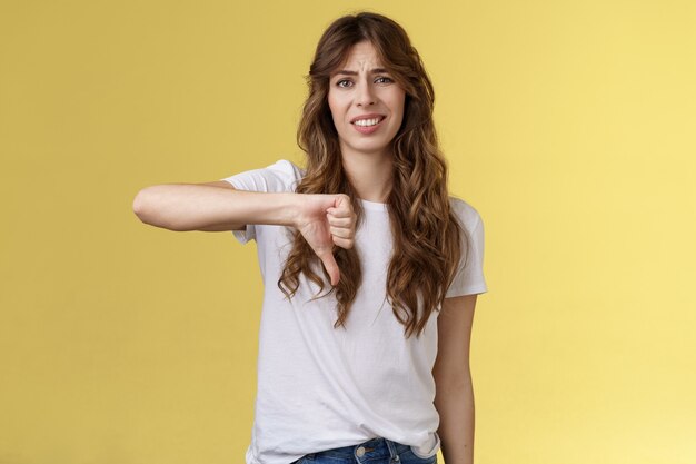 Tan cojo, perdedor. Ignorante esnob mujer guapa dar su propio juicio opinión negativa en desacuerdo haciendo muecas encogimiento aversión mostrar pulgar hacia abajo decepcionado no impresionado fondo amarillo