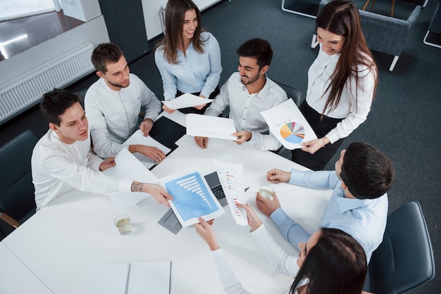 Foto gratuita tan joven pero tan exitoso. vista superior de los trabajadores de oficina en ropa clásica sentados cerca de la mesa usando una computadora portátil y documentos