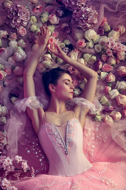 Tarde cálida. Vista superior de la hermosa joven en tutú de ballet rosa rodeada de flores. Ambiente primaveral y ternura a la luz coralina. Concepto de primavera, flor y despertar de la naturaleza.