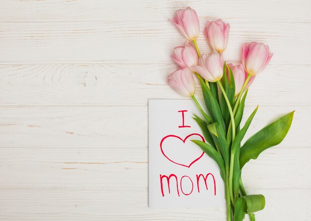 Tarjeta amo a mamá y flores colocadas en mesa de madera blanca