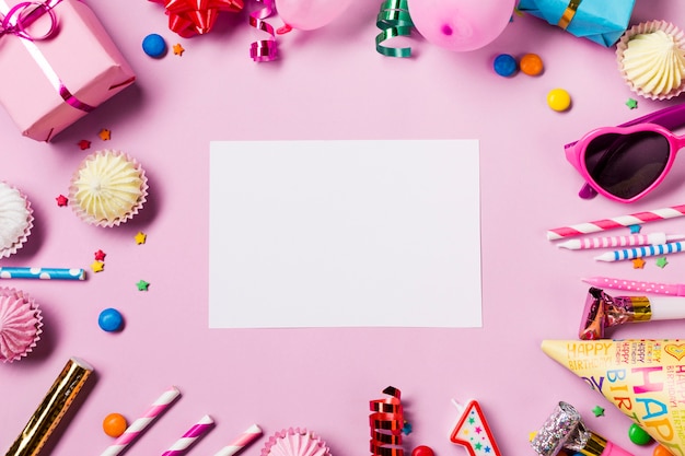 Tarjeta blanca en blanco rodeada con artículos de cumpleaños sobre fondo rosa