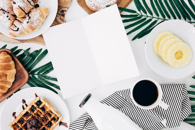 Una tarjeta en blanco abierta rodeada de desayuno en escritorio blanco