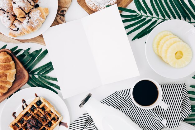 Una tarjeta en blanco abierta rodeada de desayuno en escritorio blanco