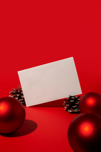 Foto gratuita tarjeta en blanco y bolas de navidad rojas y conos de pino en la mesa roja