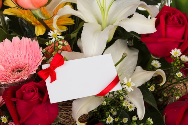 Tarjeta en blanco con cinta roja sobre flores