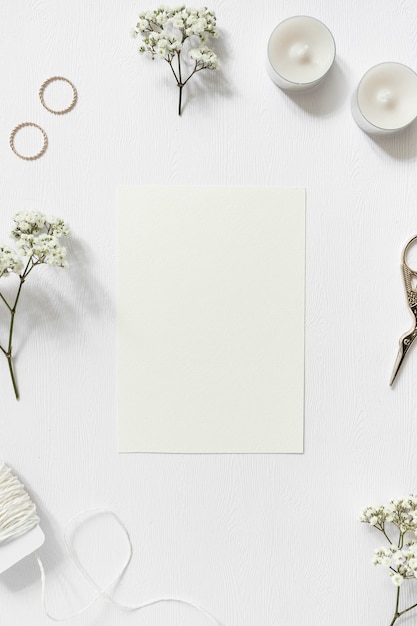 Foto gratuita tarjeta en blanco rodeada con gypsophila; anillos de boda; cadena y tijera sobre fondo blanco