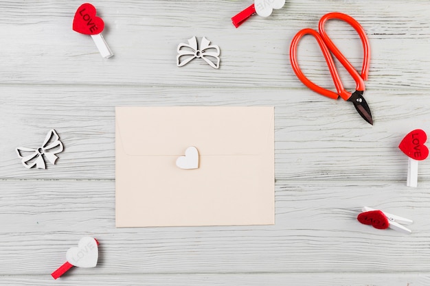 Tarjeta de felicitación rodeada con clip en forma de corazón y tijera en mesa de madera