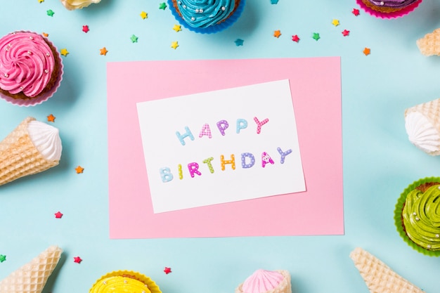 Tarjeta de feliz cumpleaños rodeada de muffins; Cono de galleta y espolvoreado sobre fondo azul