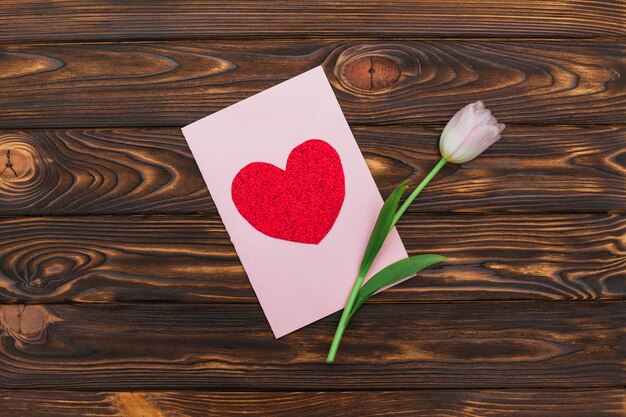 Tarjeta de San Valentín y flor en el escritorio de madera