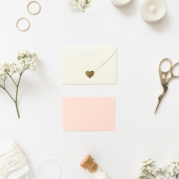 Tarjetas de felicitación en blanco rodeadas de anillos; gypsophila; cuerda; velas; Tubo de ensayo de malvavisco y tijera sobre fondo blanco