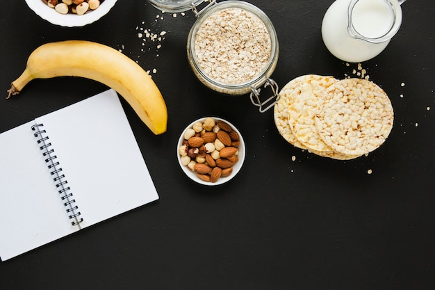 Foto gratuita tarro de avena plano con nueces, mezcla de plátano y cuaderno