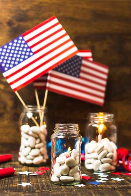 Tarro de caramelos blanco con velas encendidas y bandera de Estados Unidos en el escritorio de madera