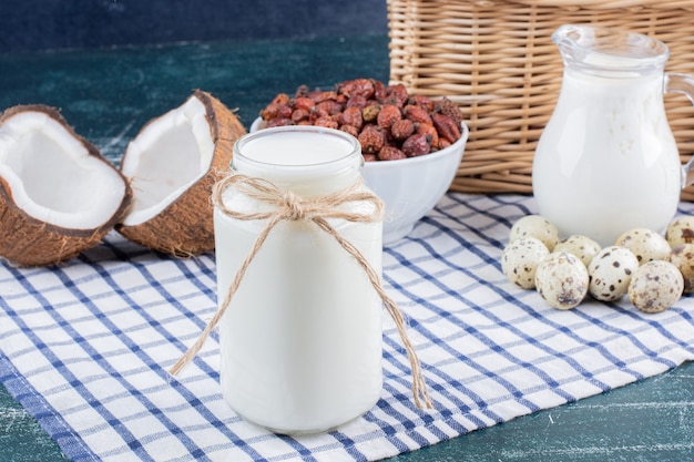 Tarro de cristal de leche, dátiles secos y huevos de codorniz sobre mesa de mármol.