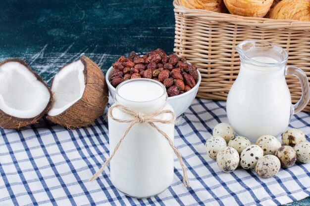 Tarro de cristal de leche, dátiles secos y huevos de codorniz sobre mesa de mármol.