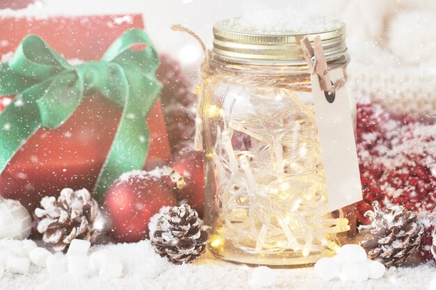 Tarro de cristal con luces y adornos navideños con nieve alrededor