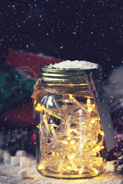 Tarro de cristal con luces con un regalo al lado mientras nieva