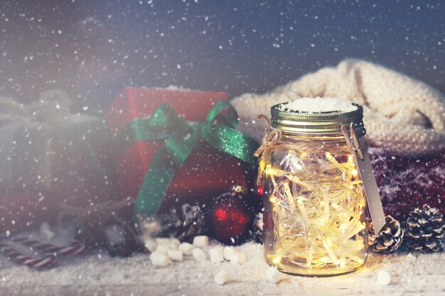 Tarro de cristal con luces con un regalo al lado mientras nieva