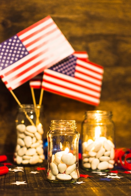 Tarro de dulces rellenos con velas encendidas y banderas de los Estados Unidos en mesa de madera