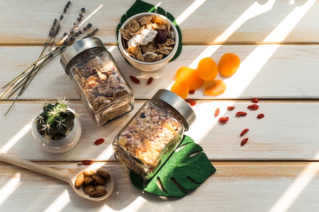 Tarro de granola y copos de maíz cerca de frutos secos sobre fondo de madera