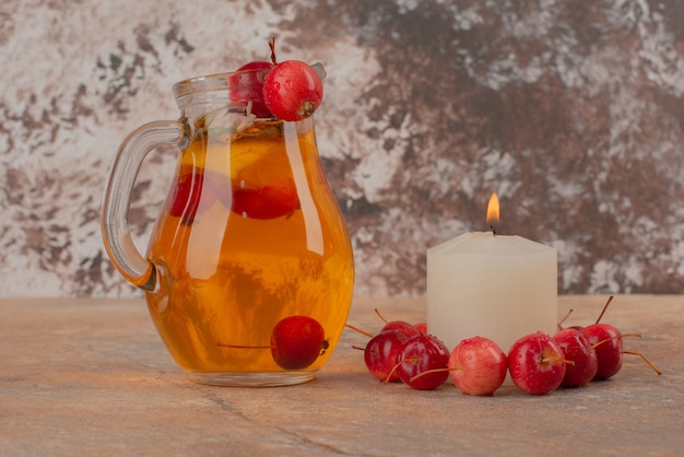 Un tarro de jugo de durazno con cerezas y velas en la mesa de mármol.