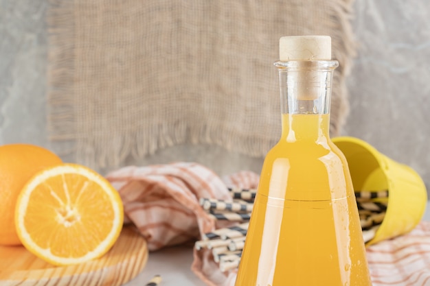 Tarro de jugo de naranja con naranjas frescas sobre superficie de mármol