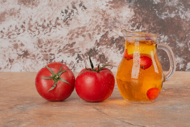 Un tarro de jugo y tomates frescos en la mesa de mármol.