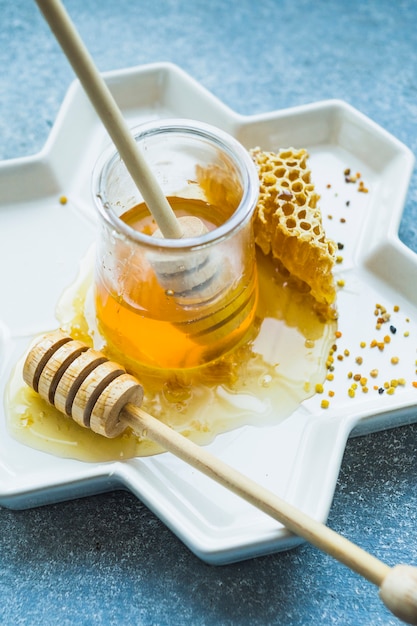 Tarro de miel con cucharón de miel y peine de miel en bandeja floral