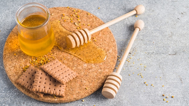 Tarro de miel; galletas; cucharón de miel de madera y polen de abeja en el fondo de hormigón