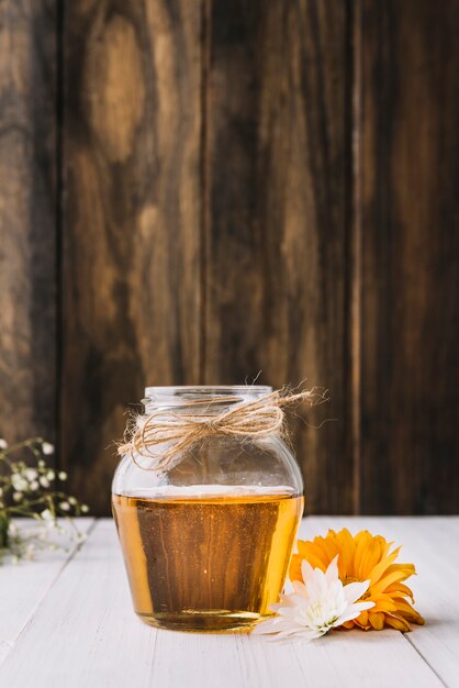 Tarro de miel con hermosas flores en superficie de madera