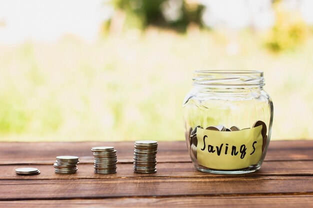 Tarro con pila de ahorros y monedas en la mesa