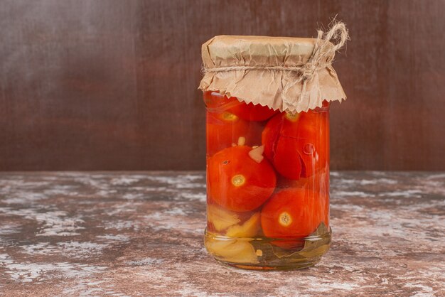 Tarro de tomates encurtidos caseros sobre mesa de mármol.