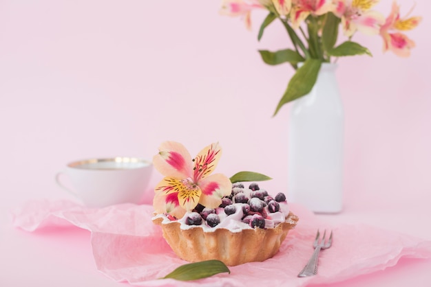 Tarta de arándanos decorada con flor de alstroemeria sobre fondo rosa